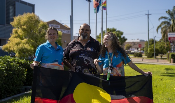 three people smiling outside holding large Aboriginal flag