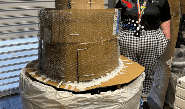 person standing next to large cardboard cake structure