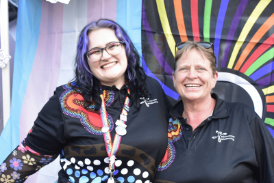 two people smiling in front of rainbow flags