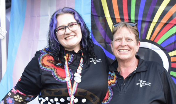 two people smiling in front of rainbow flags