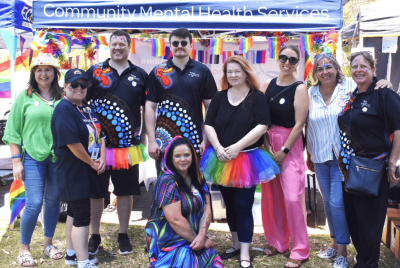 Nine people standing together in rainbow outfits and face paint