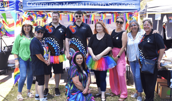 Nine people standing together in rainbow outfits and face paint