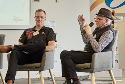 two men sitting and talking to a crowd