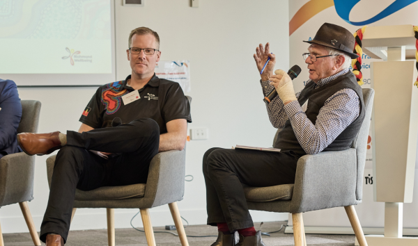 two men sitting and talking to a crowd