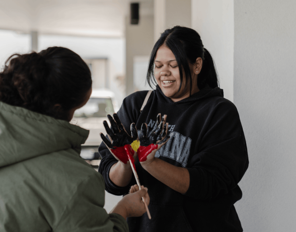 Person with their hands out in front of them being painted with the Aboriginal Flag