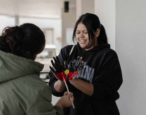 Person with their hands out in front of them being painted with the Aboriginal Flag